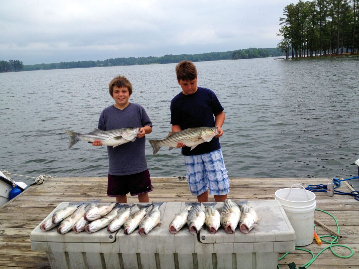 Two boys holding up fish on a dock.